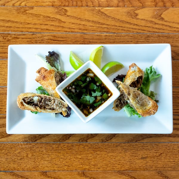 Crispy fried egg rolls with a savory filling, served with a dipping sauce and lime wedges.