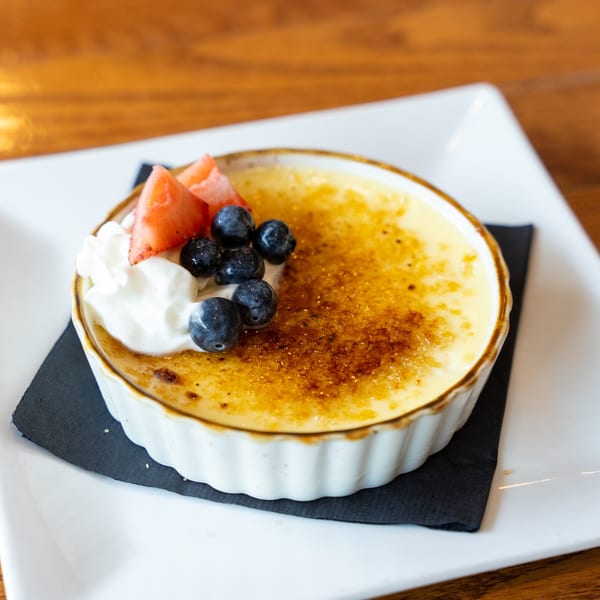 Crème brûlée in a white ramekin, topped with whipped cream, blueberries, and sliced strawberries.