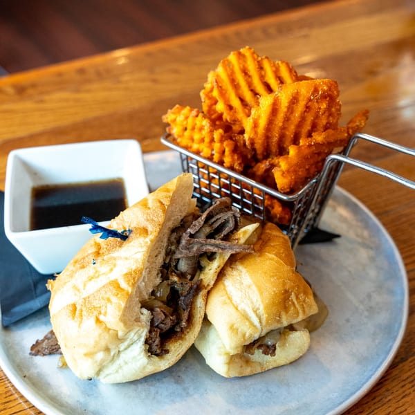 French dip sandwich with waffle fries and au jus on a light blue plate.